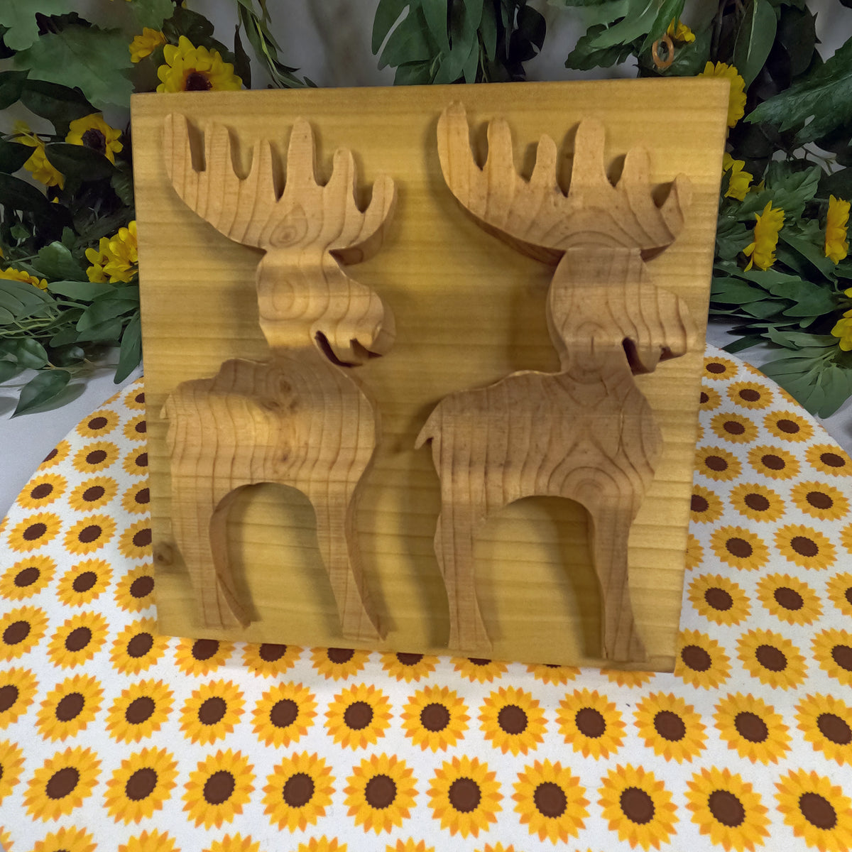 Wooden moose-shaped cutouts on a wooden board with a sunflower-patterned tablecloth.
